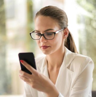 Professional woman using smartphone while working on laptop in modern office.