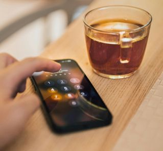 Close-up of hand unlocking a smartphone next to a cup of tea on a wooden table, emphasizing technology and security.